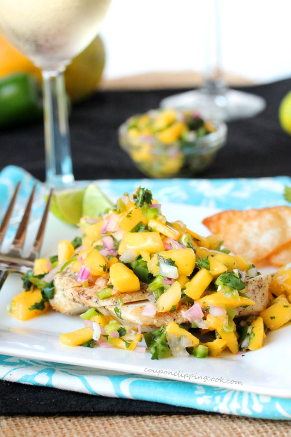 Grilled chicken covered in mango salsa on a white plate