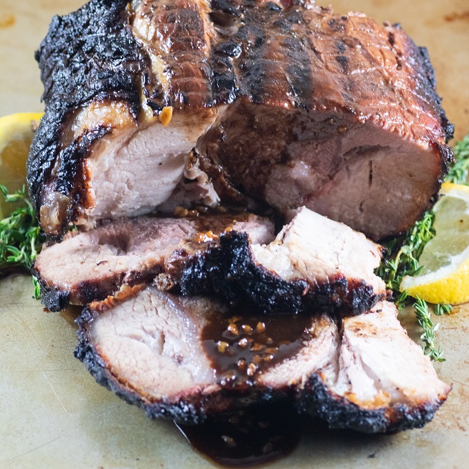 Sliced Marinated BBQ Pork Roast with lemon wedges and thyme sprigs