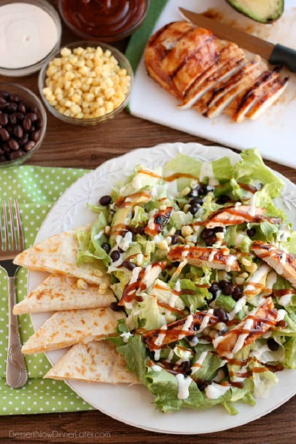 Grilled chicken slices on a bed of lettuce with pita triangles on a white plate with corn and black beans