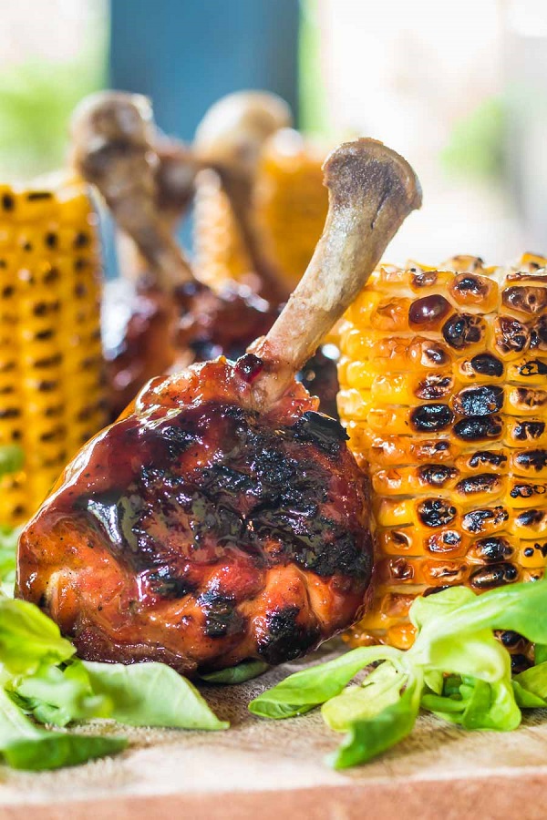 Chicken Drumstick on a wooden board with grilled corn on the cob and lettuce