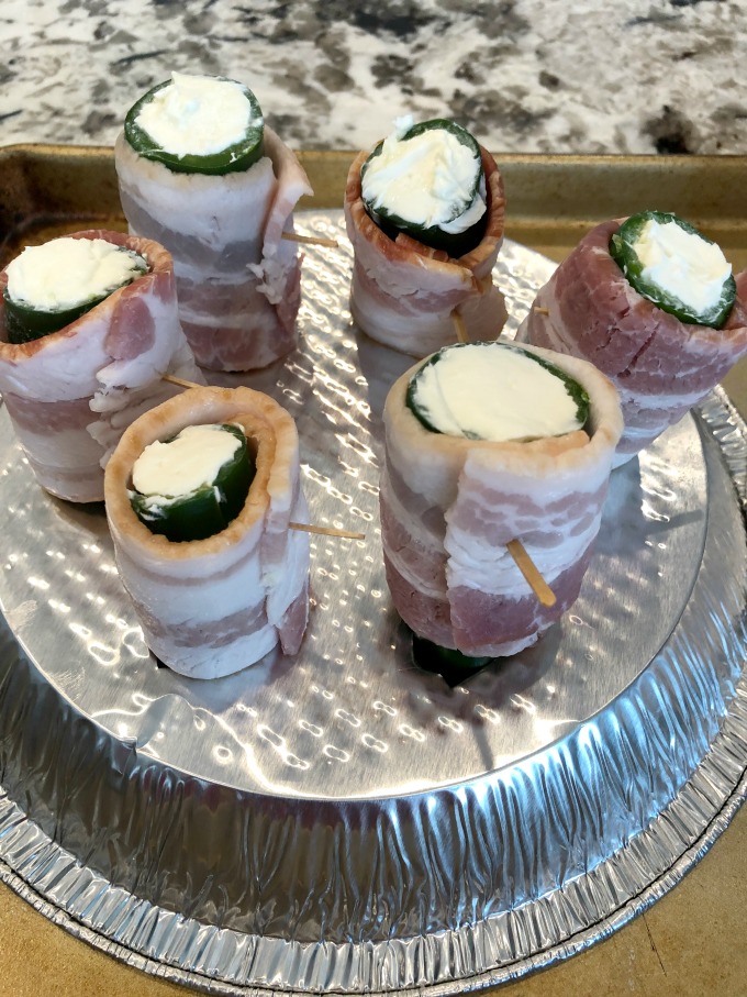 Prepared bacon wrapped, cream cheese stuffed jalapeno poppers standing on the homemade foil pie plate stand