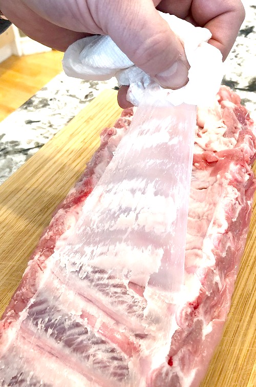 Removing the membrane from the rack of ribs with a dry paper towel sitting on a cutting board