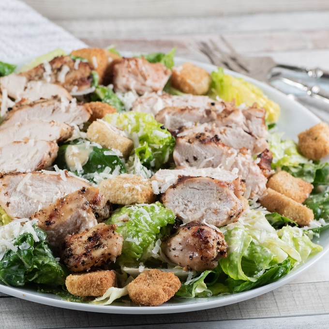 Grilled Chicken Caesar Salad on a white plate with croutons and grated parmesan cheese