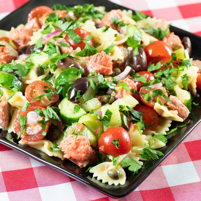 Grilled Pasta Salad on a black plate on top of a red and white tablecloth 