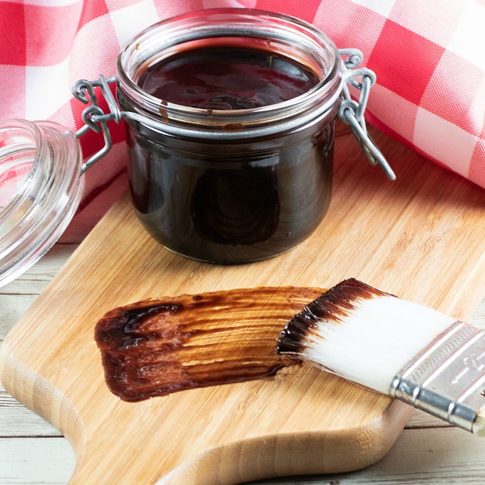 Jar of BBQ Sauce on a board with a brush and a smear of BBQ sauce on the board