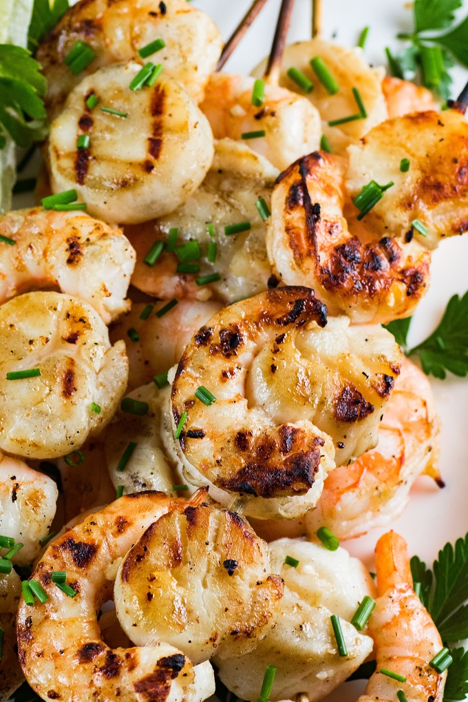 Grilled scallops and shrimp on wooden skewers with chives and parsley
