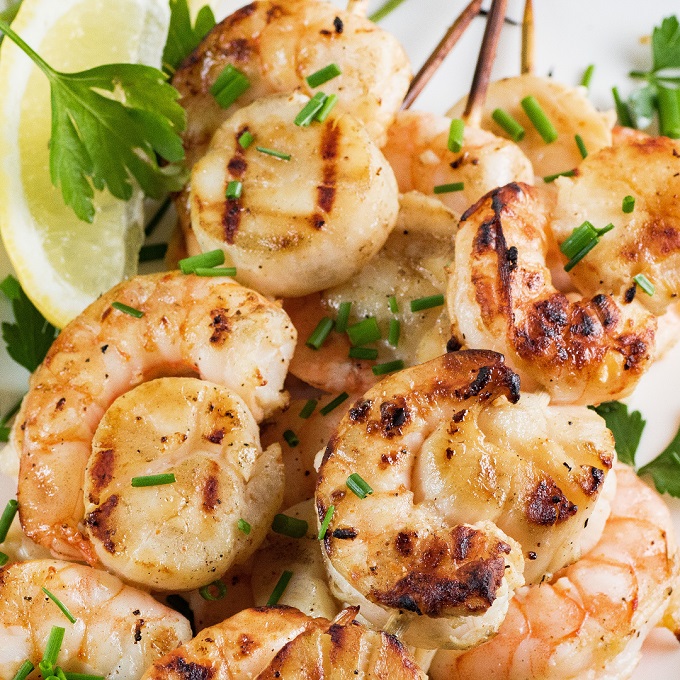 Grilled scallops and shrimp on wooden skewers with chopped chives, parsley and lemon wedge