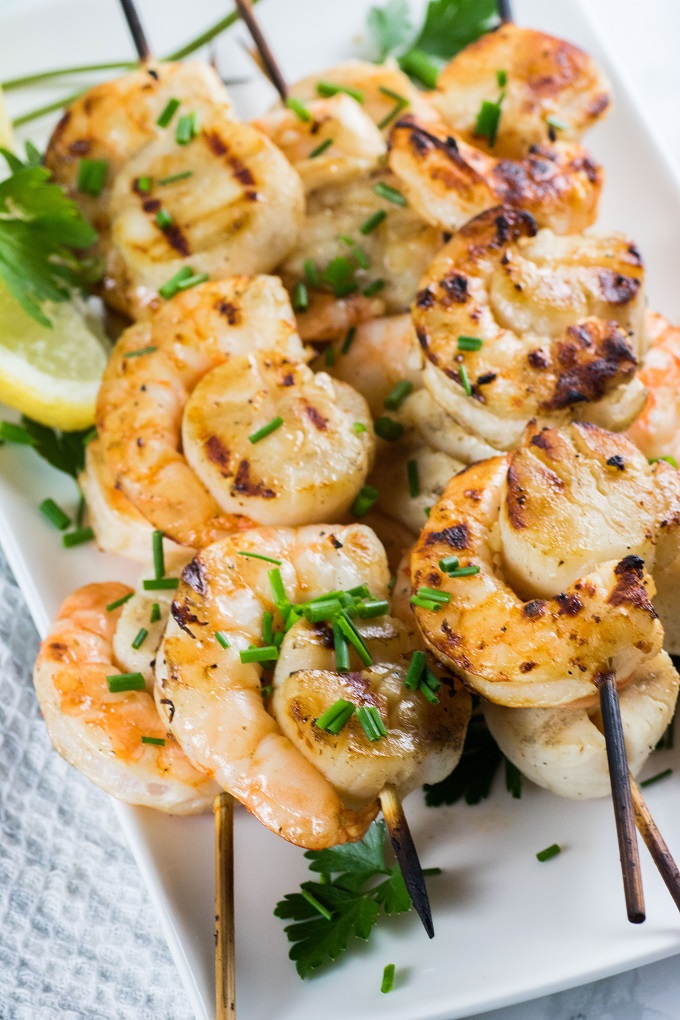 Grilled scallop and shrimp skewers on a white plate with chopped chives and parsley
