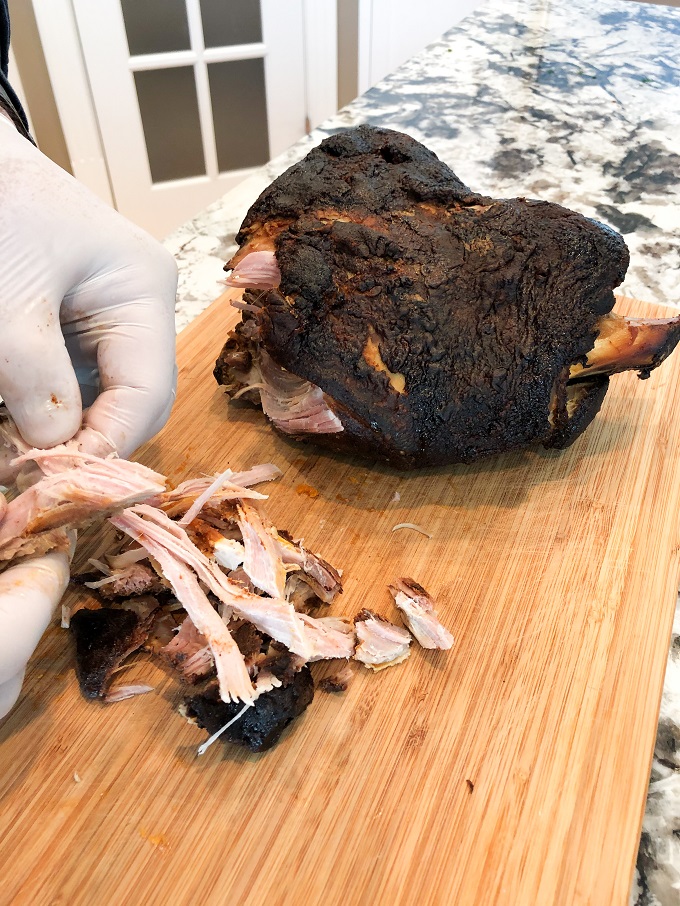 Hand shredding the Smoked Pork Shoulder on a wooded cutting board