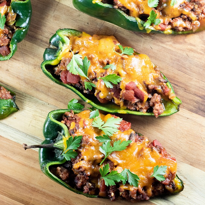 2 stuffed poblano peppers on a wooden cutting board