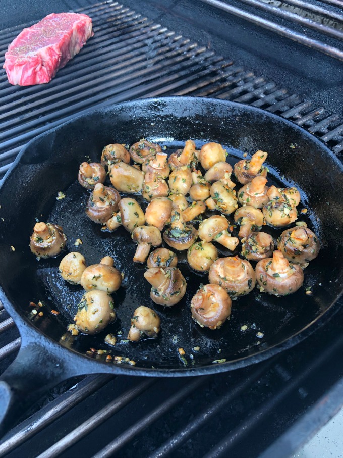 Cast Iron fry pan on the grill sauteing the mushrooms, with the steak cooking in the background