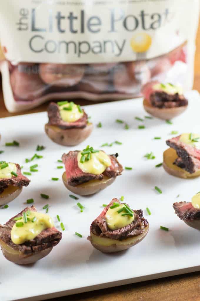 Little potato halves topped with a slice of grilled steak and bernaise sauce on a white board
