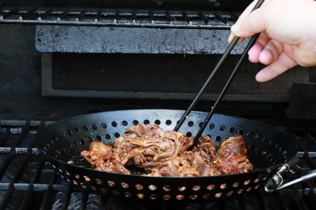 Beef being cooked in a grill basket on a grill.