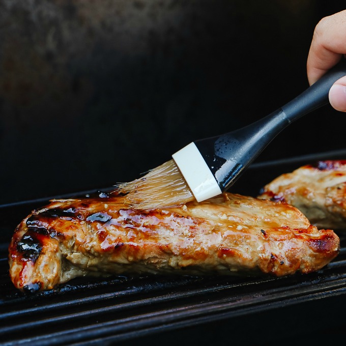 Teriyaki pork tenderloin on the grill being brushed with glaze