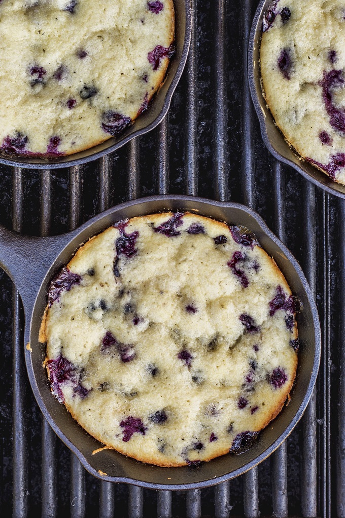 Lemon blueberry cakes in small cast iron fry pans cooking on the grill.