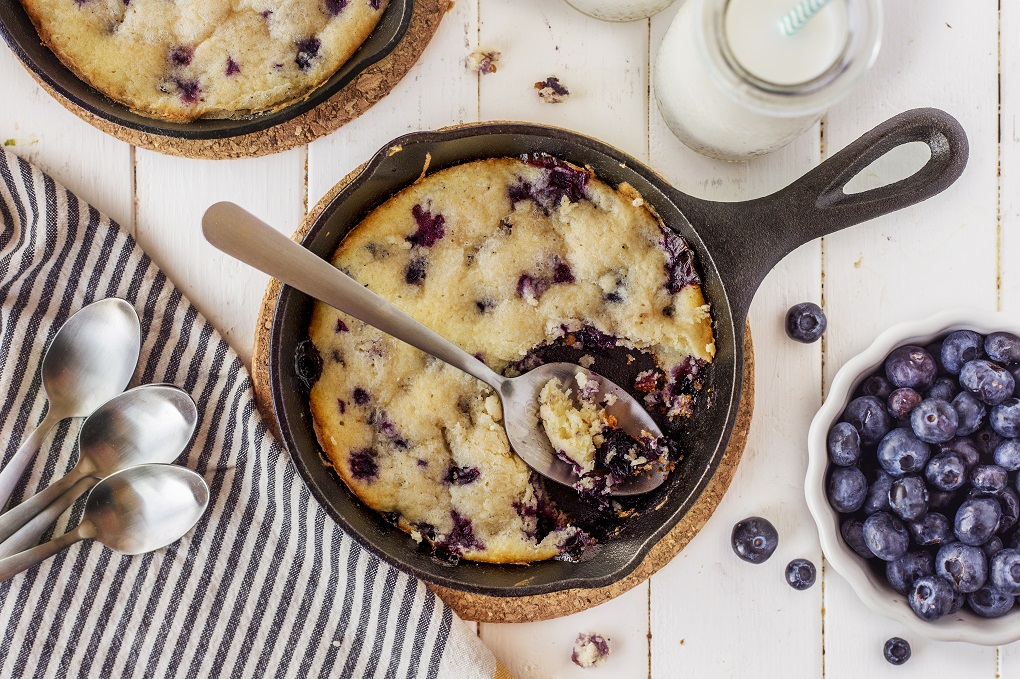 Lemon Blueberry cake in a small cast iron pan with a spoon that is full of cake 