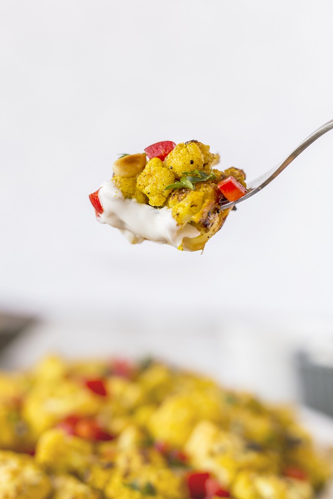 Curry grilled cauliflower floret on a fork with sour cream, red pepper and ttoasted pine nut