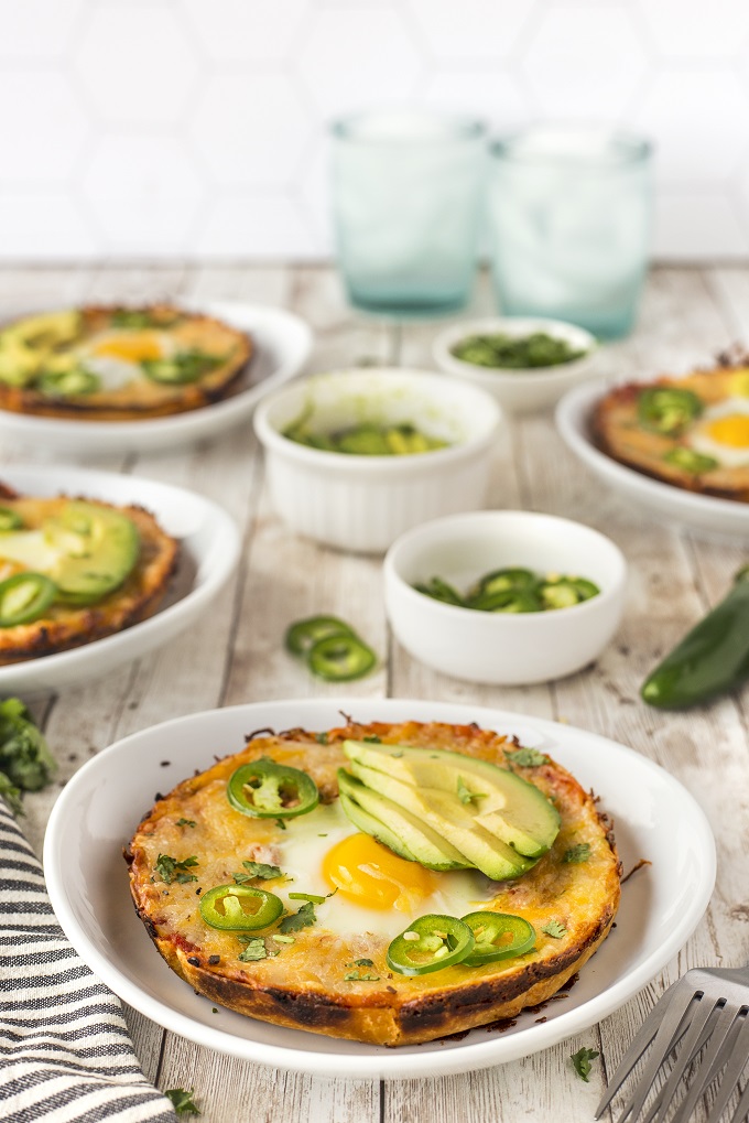 Individual Huevos Rancheros in a white plate, garnished with adocado and jalapeno slices and chopped cilantro