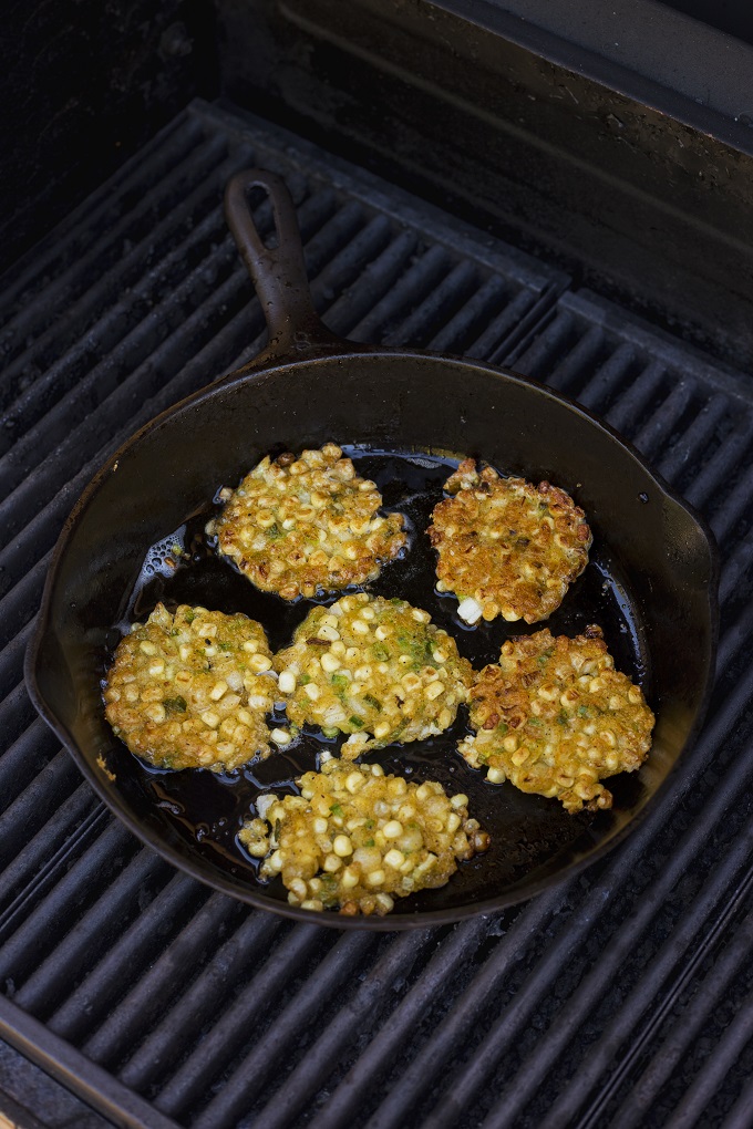 Corn fritter patties frying in a cast iron skillet on the grill