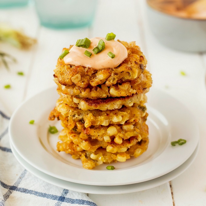 Close up of a stack of corn fritters on a small white plate with a dollop of spicy dipping sauce on top.