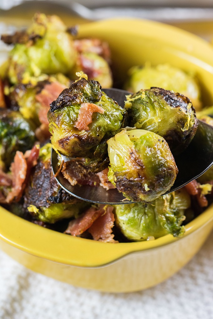 Grilled brussel sprouts ona serving spoon with a bowl of them in the background.