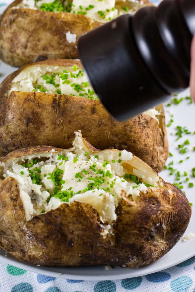 Baked potatoes on a white plate with butter, chives and black pepper