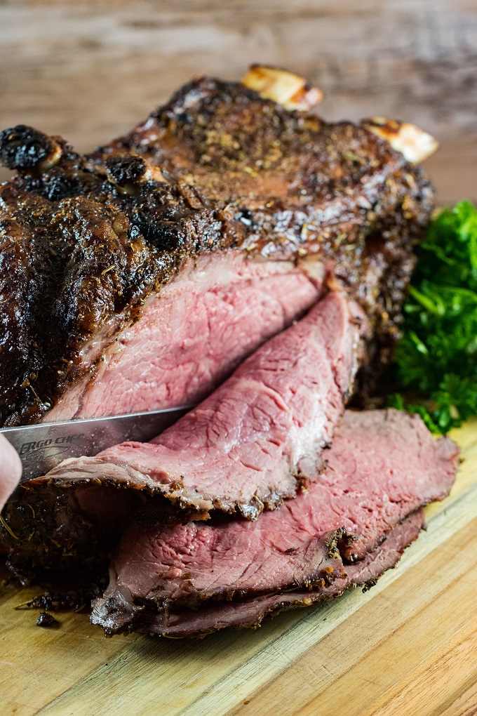 Prime rib being sliced on a wooden cutting board.
