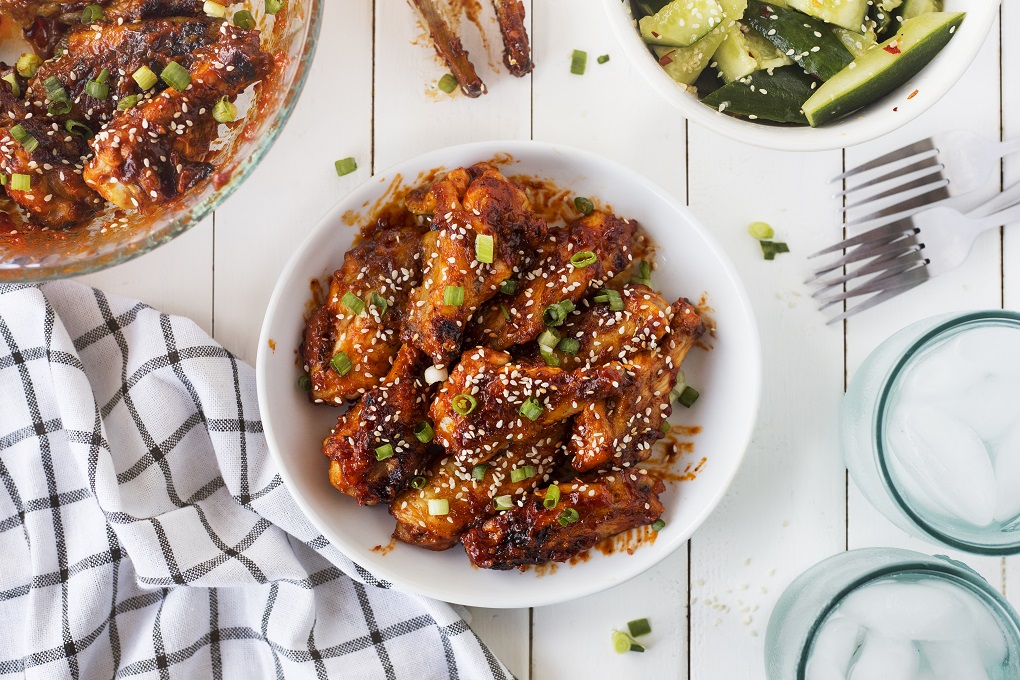 Korean Chicken Wings on a small white serving plate with a large bowl of the wings beside, on a white board