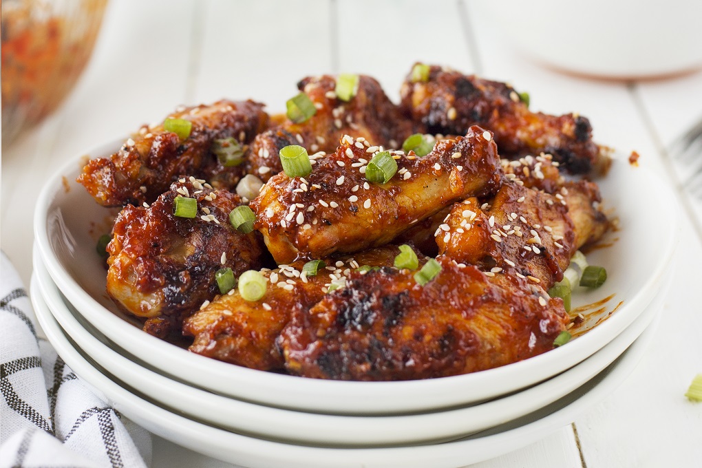 Saucy Korean chicken wings stacked on a white plate with green onions and sesame seeds sprinkled on top