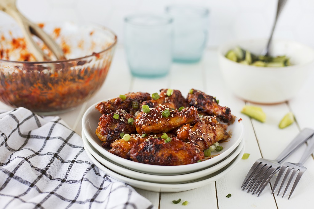 Grilled Korean chicken wings on a small white plate with forks, garnished with sesame seeds and sliced green onions