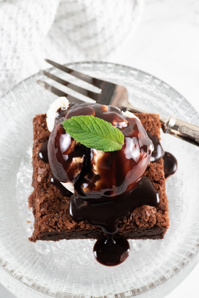 BBQ nutella chcolate brownie on a glass plate with a scoop of ice cream and a drizzle of chocolate sauce garnishd iwth a mint leaf