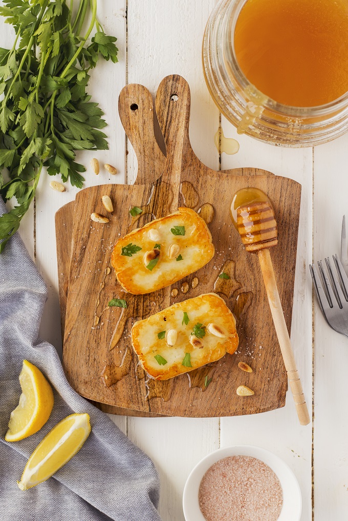 Smoked fried Halloimi slices on a wooden cutting board with honey and toasted pine nuts.