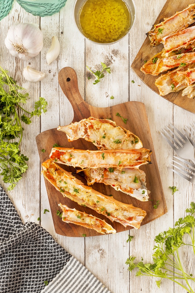 Grilled crab legs on a wooden cutting board with chopped parsley as a garnish