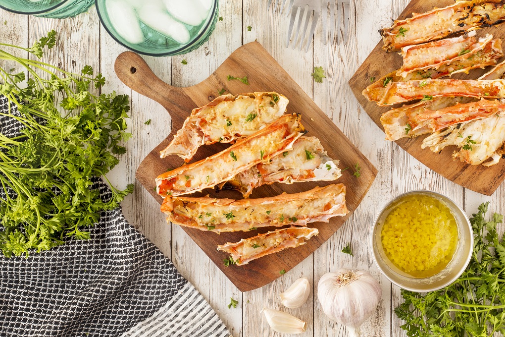 Grilled king crab legs on a wooden cutting board with garlic butter and parsley