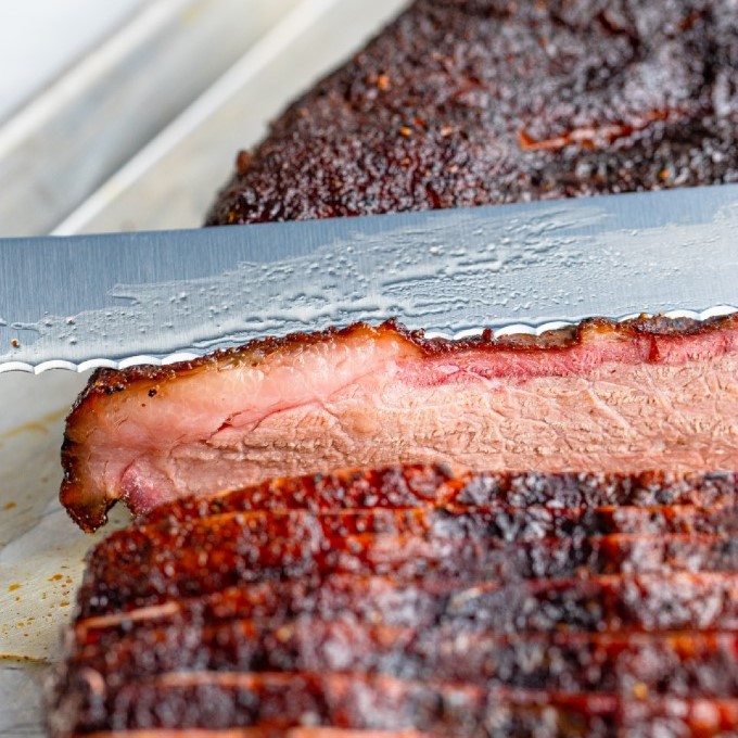 close up of a knife slicing smoked brisket