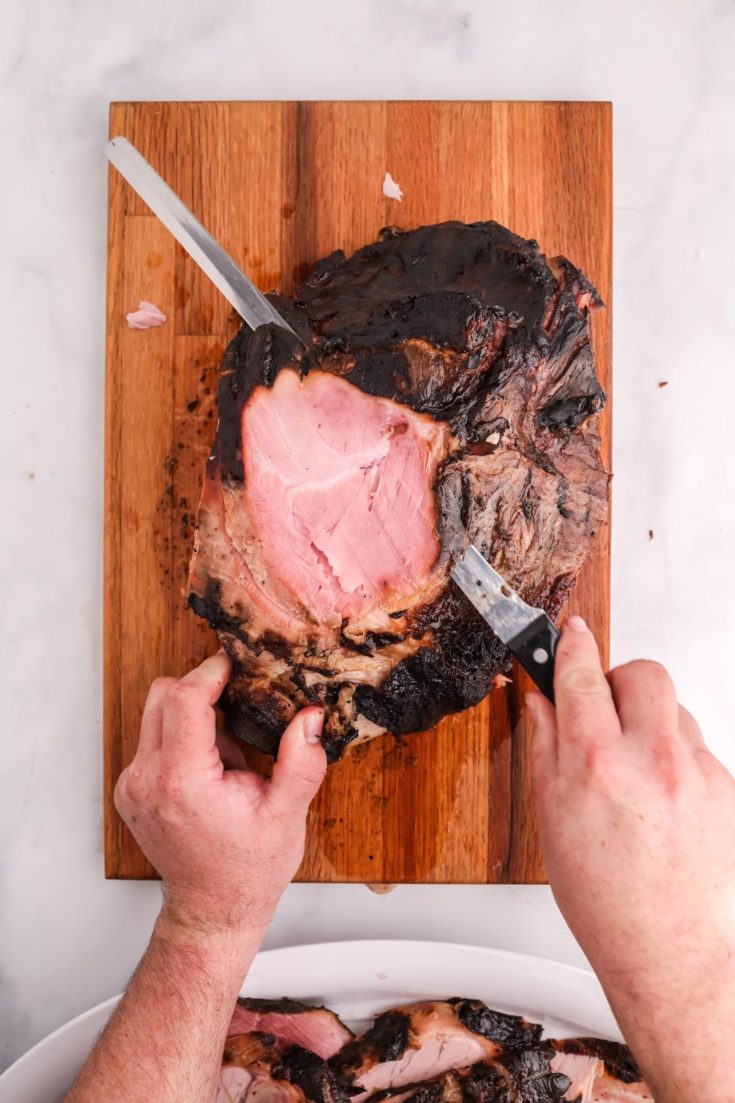 Smoked bone in ham leg being sliced on a wooden cutting board