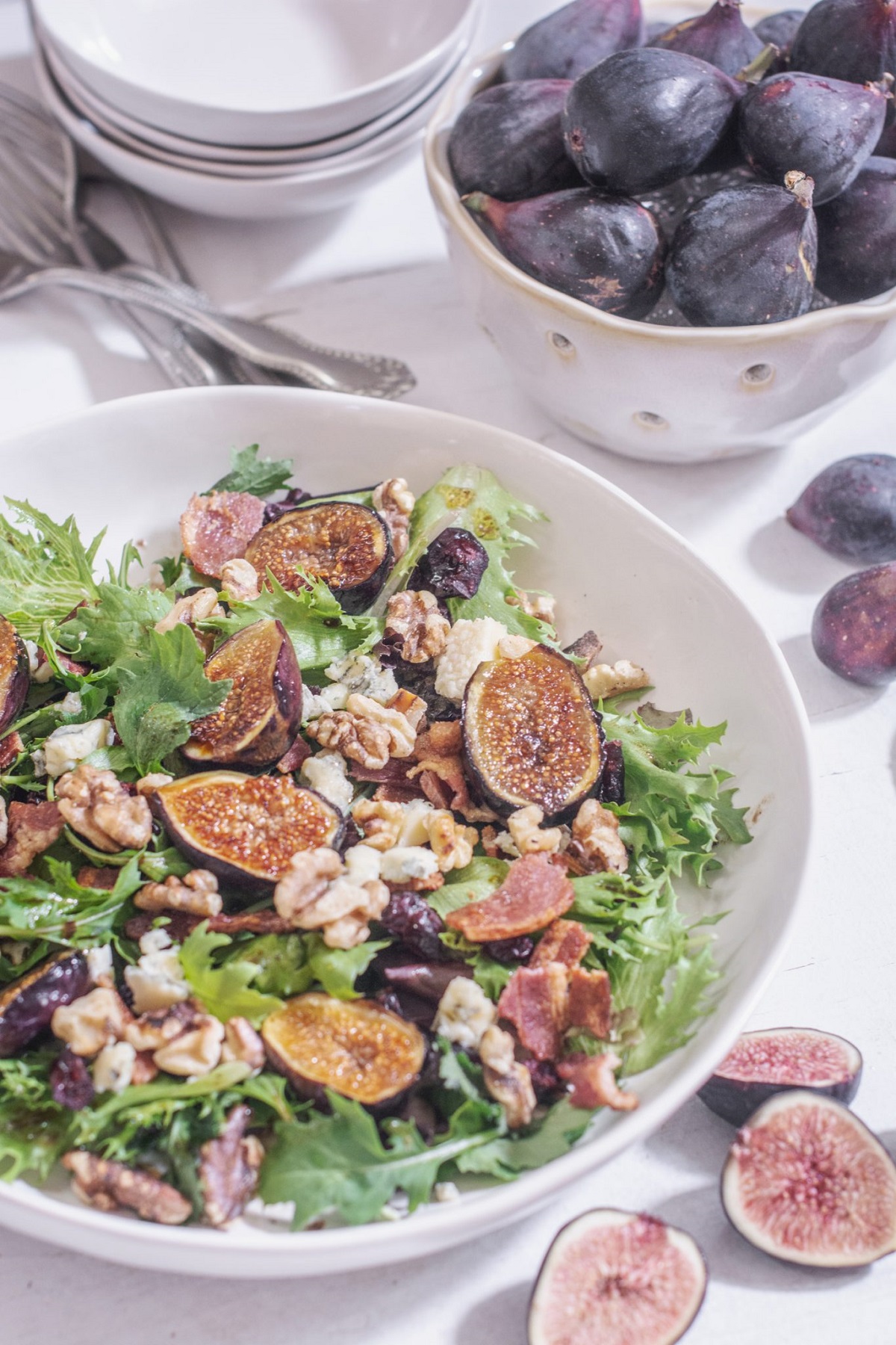 Grilled fig salad on a white serving platter with sliced figs beside the bowl.