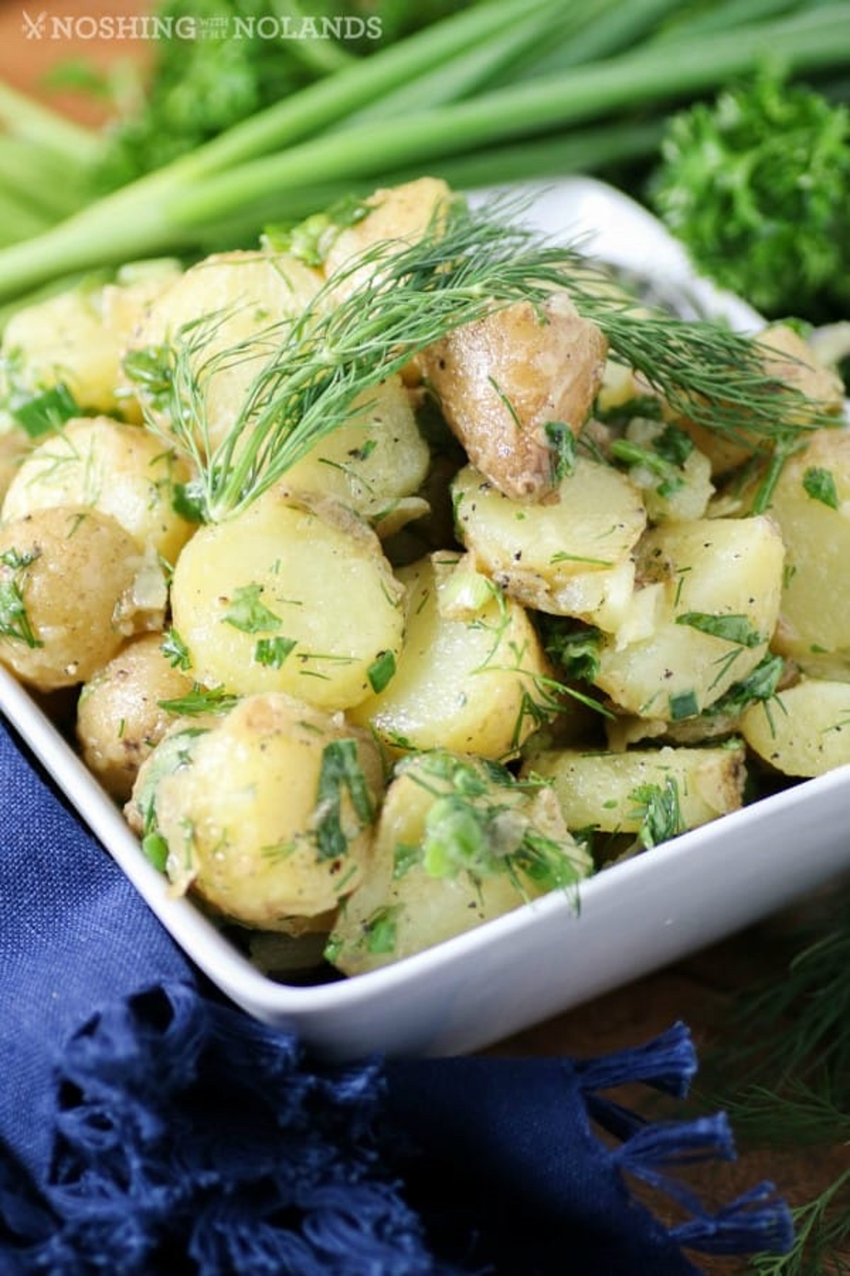 Herbed potato salad in a white serving bowl with parsley, chives and dill.