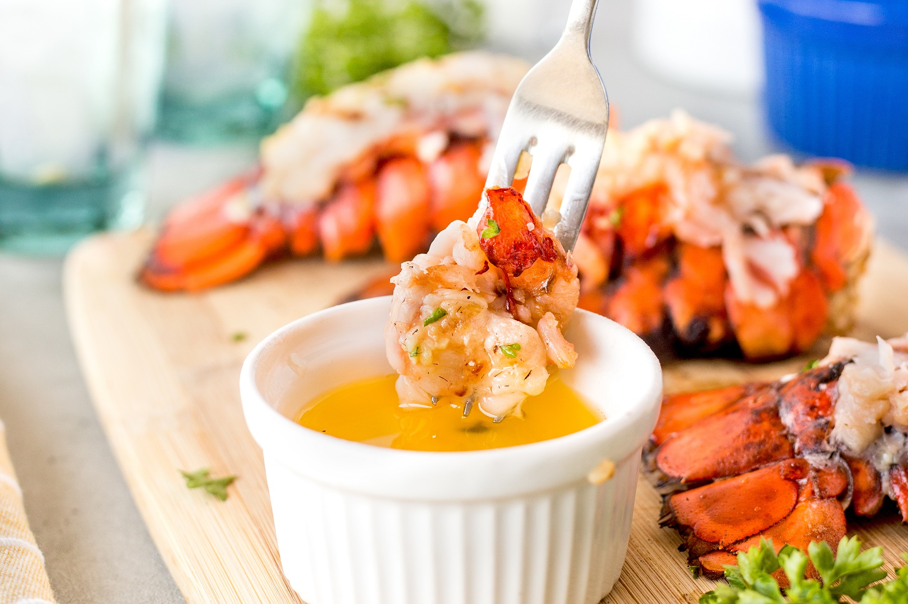 Fork full of grilled lobster being dipped into a small white bowl of melted butter.