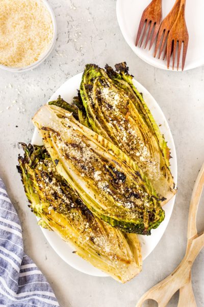 Grilled romaine lettuce halves on a white patter with grated cheese sprinkled on top