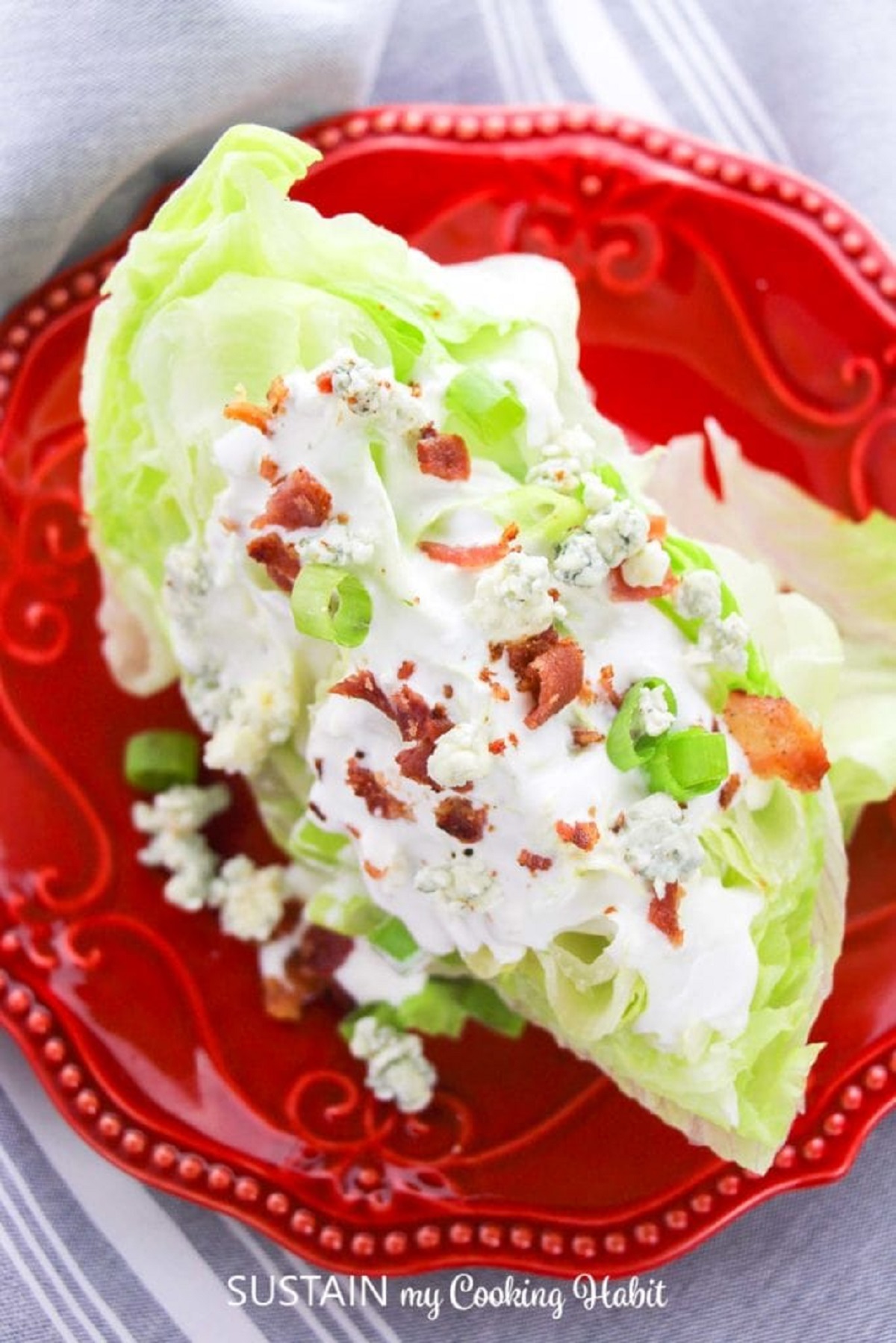 Wedge of iceberg lettuce covered in dressing and bacon bits on a bright red plate.