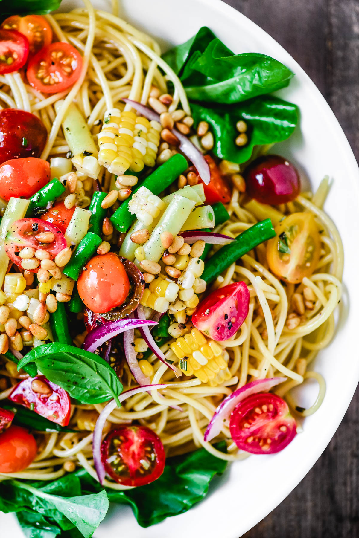 Spaghetti salad with baby tomatoes, corn, roasted pine nuts red onion and garnished with whole basil leaves.