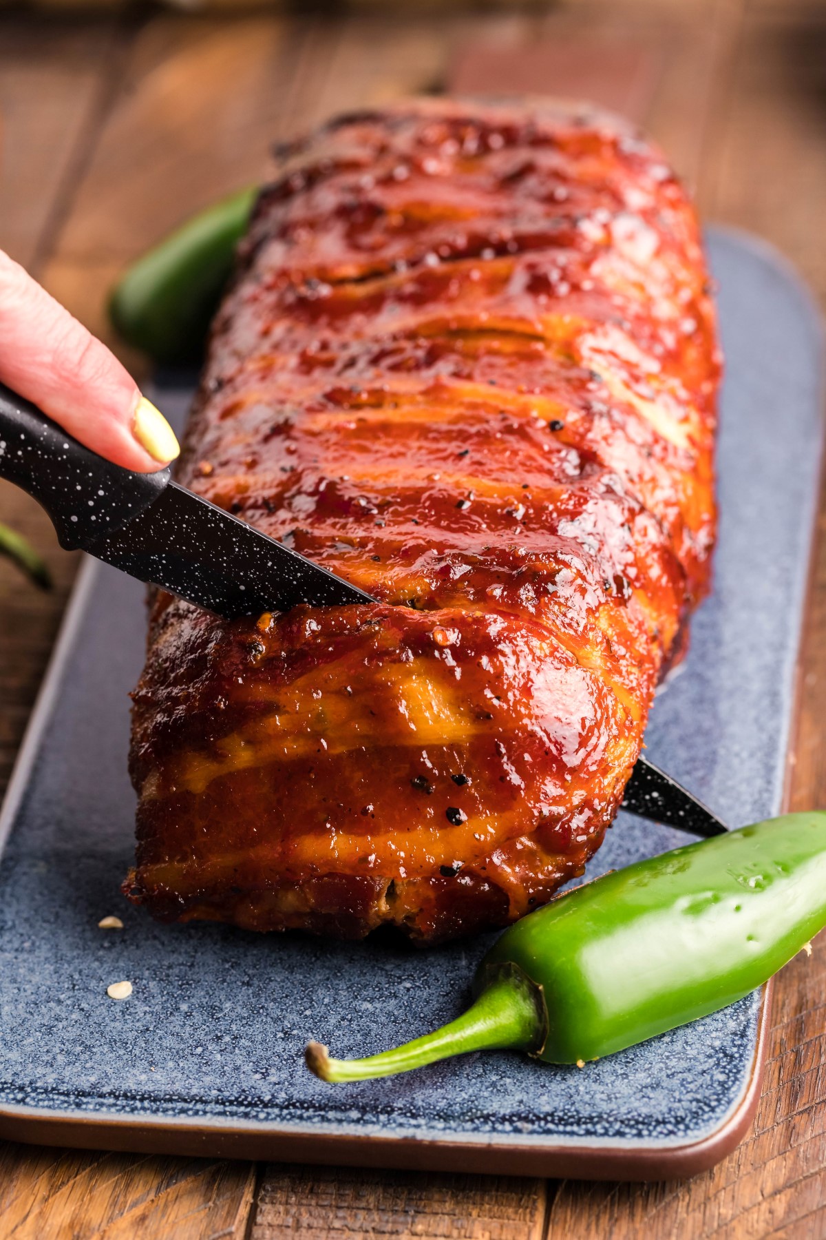 Bacon wrapped sausage roll on a stone cutting board with a knife cutting a slice off the end.