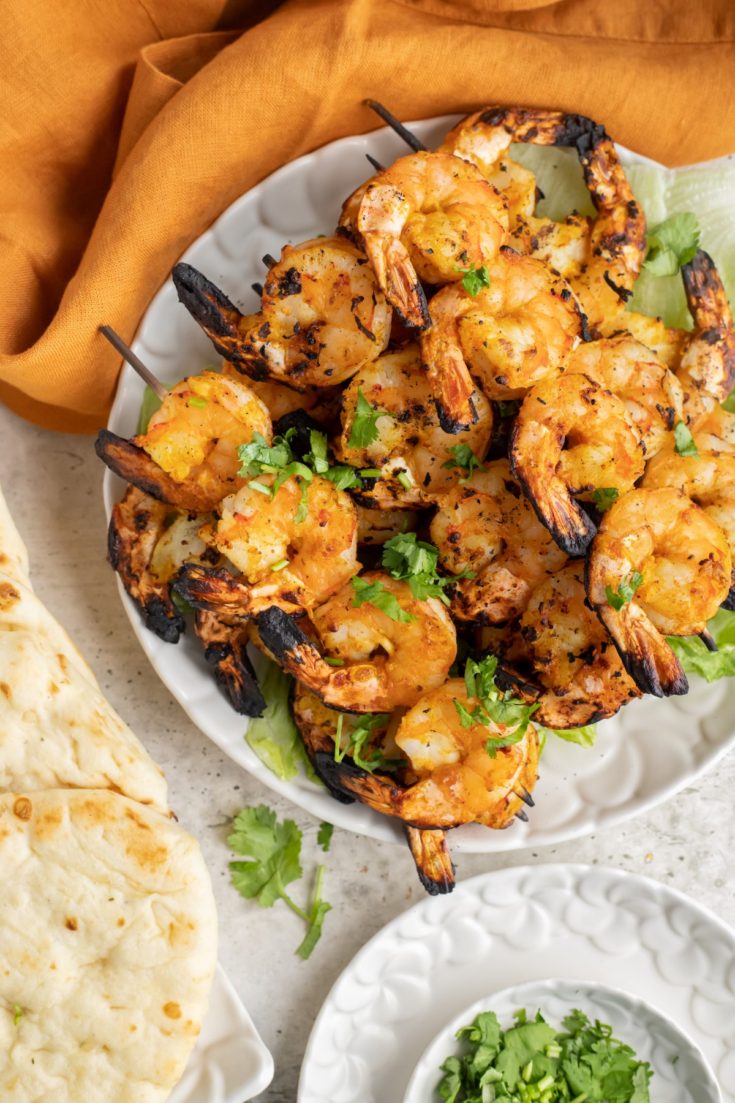 Grilled Tandoori shrimp skewers ona white plate with naan bread