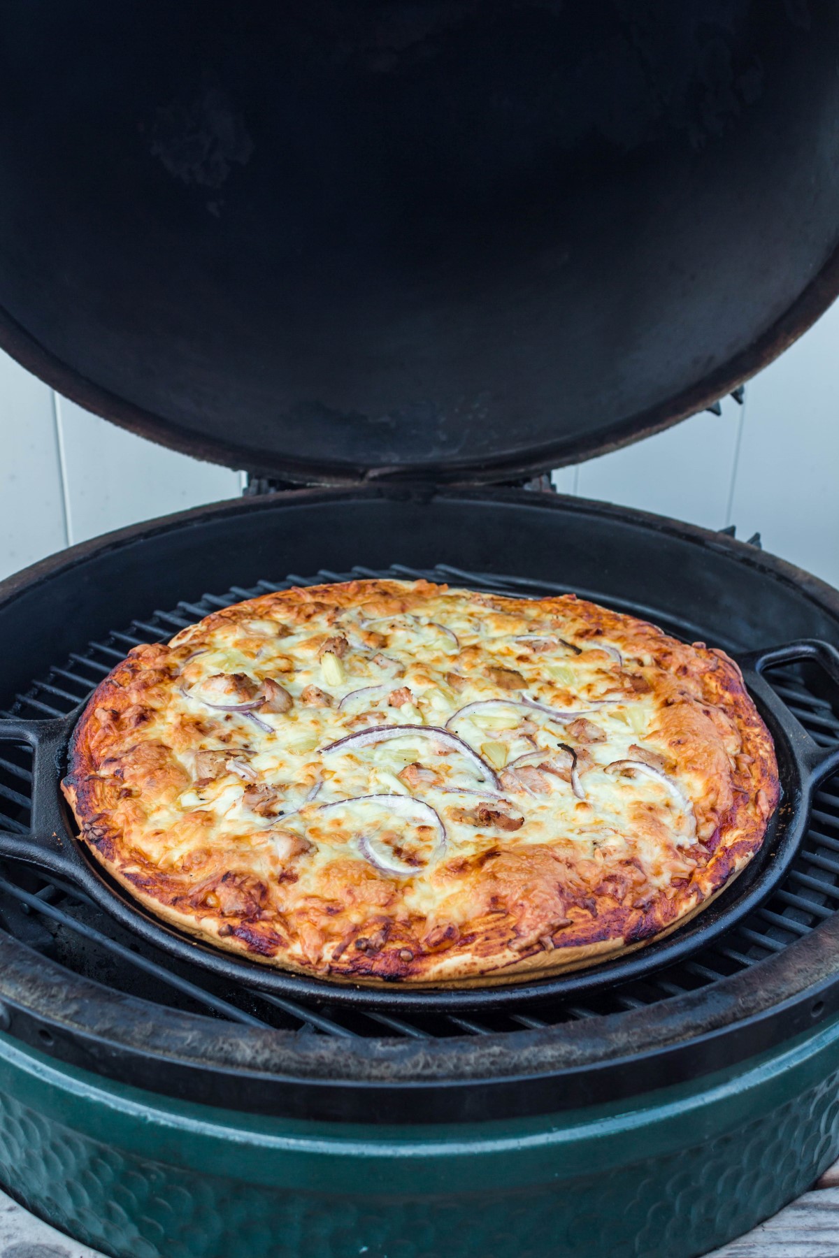BBQ chicken pizza cooking on the grill in a cast iron pizza pan