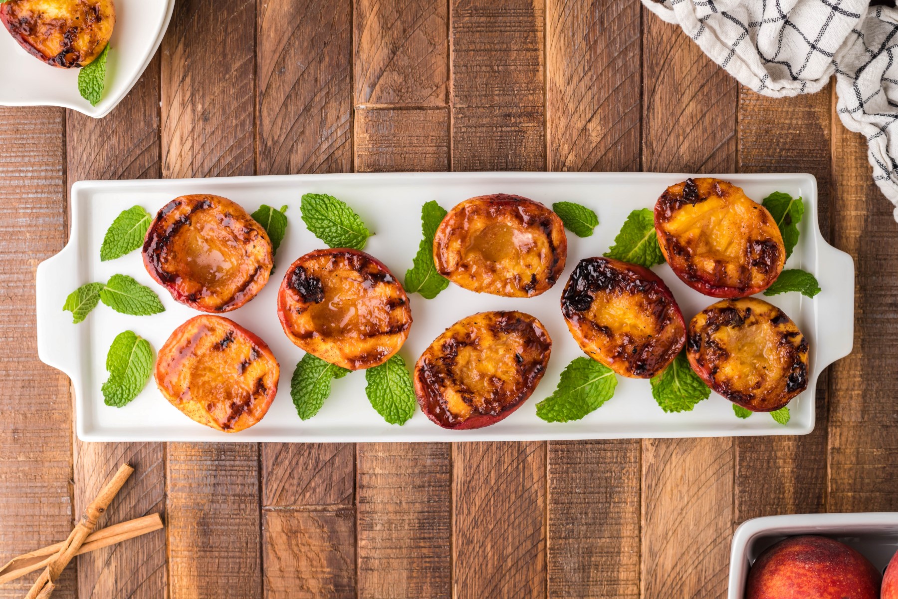 Grilled peach halves on a white platter with mint leaves.