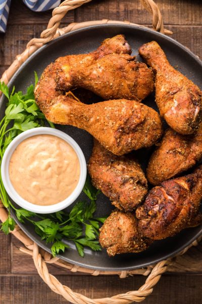 Smoked chicken drumsticks covered in dry rub on a black serving platter with Chipotle Aioli dipping sauce in a small bowl.