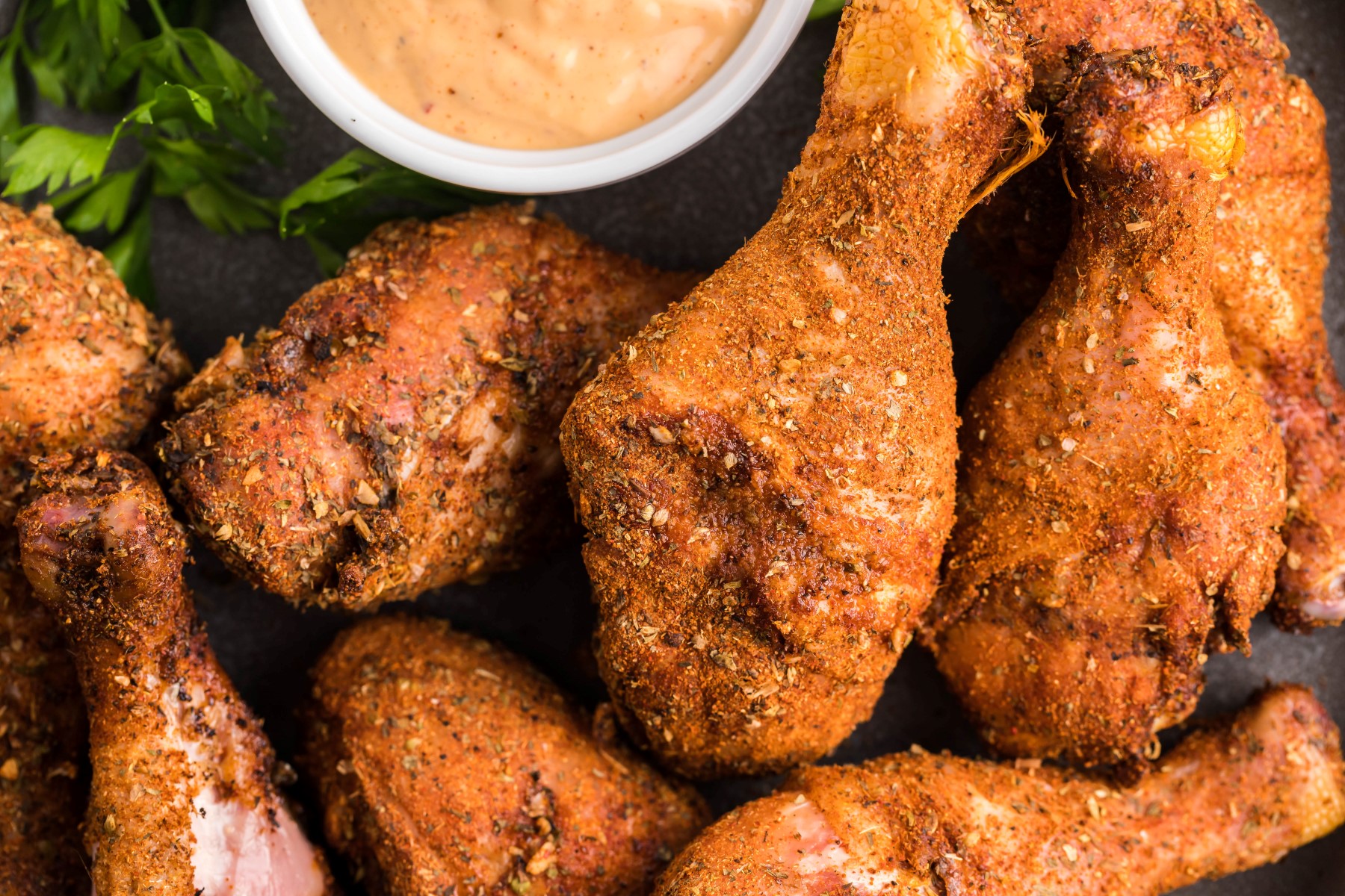 Dry Rub smoked chicken drumsticks on a dark platter with a small bowl of chipotle aioli 