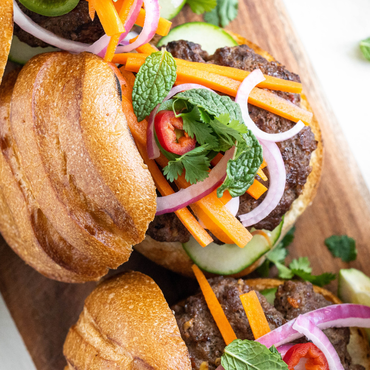 Banh Mi burgers topped with pickled veggies on a wooden board