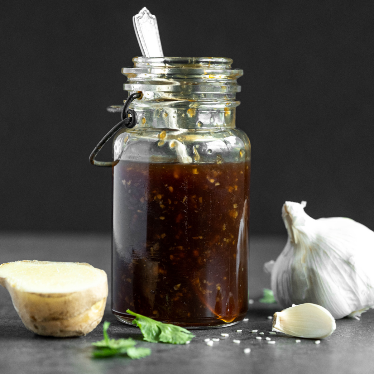 Glass jar of teriyaki sauce with a clove of garlic and piece of ginger beside the jar.